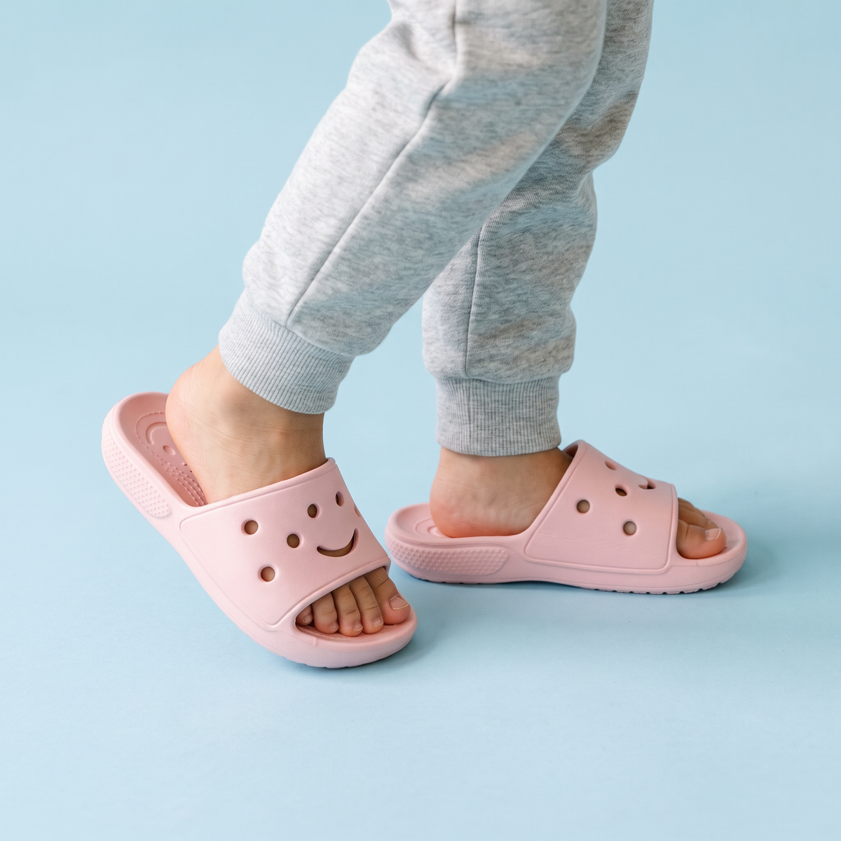 Pés de criança usando o Chinelo Slide Infantil Gummie rosa claro sobre fundo azul bebê