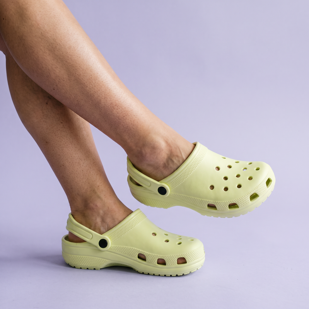 Pés usando o Clog Adulto Gummie verde-claro sobre fundo lilás