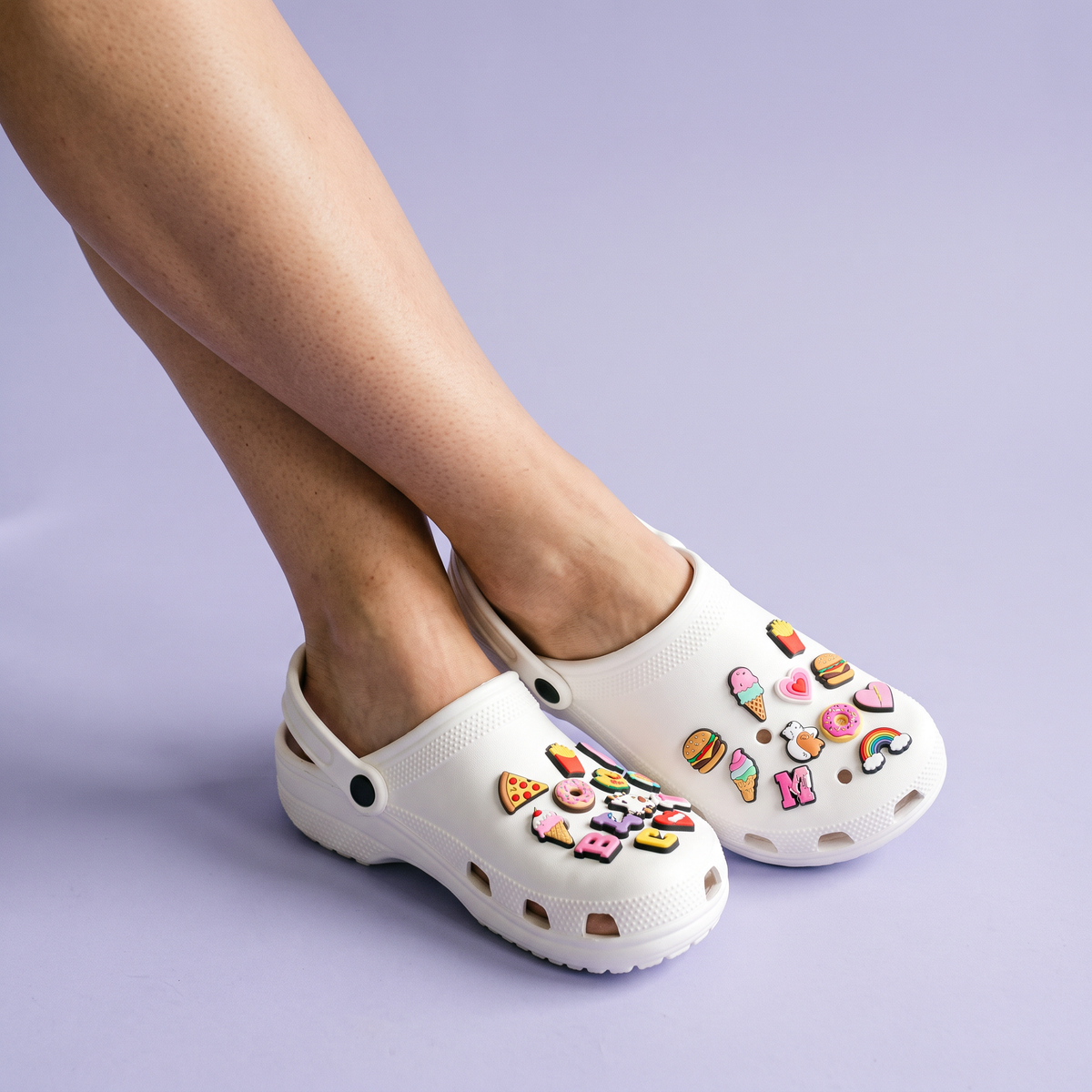 Pés usando clog branca com Gominhas coloridas sobre fundo lilás