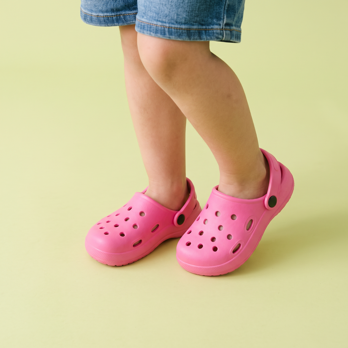 Pés de criança usando o Clog Infantil Básica rosa sobre fundo verde-limão