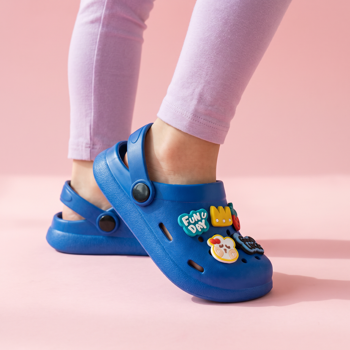 Pés de criança usando o Clog Infantil Fun Day azul sobre fundo rosa