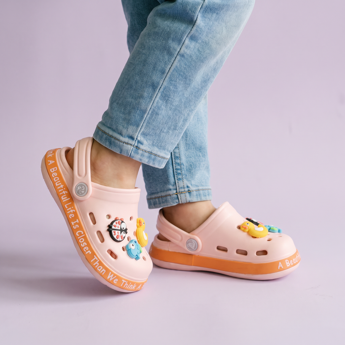 Pés de criança usando o Clog Infantil Zoo rosé sobre fundo lilás